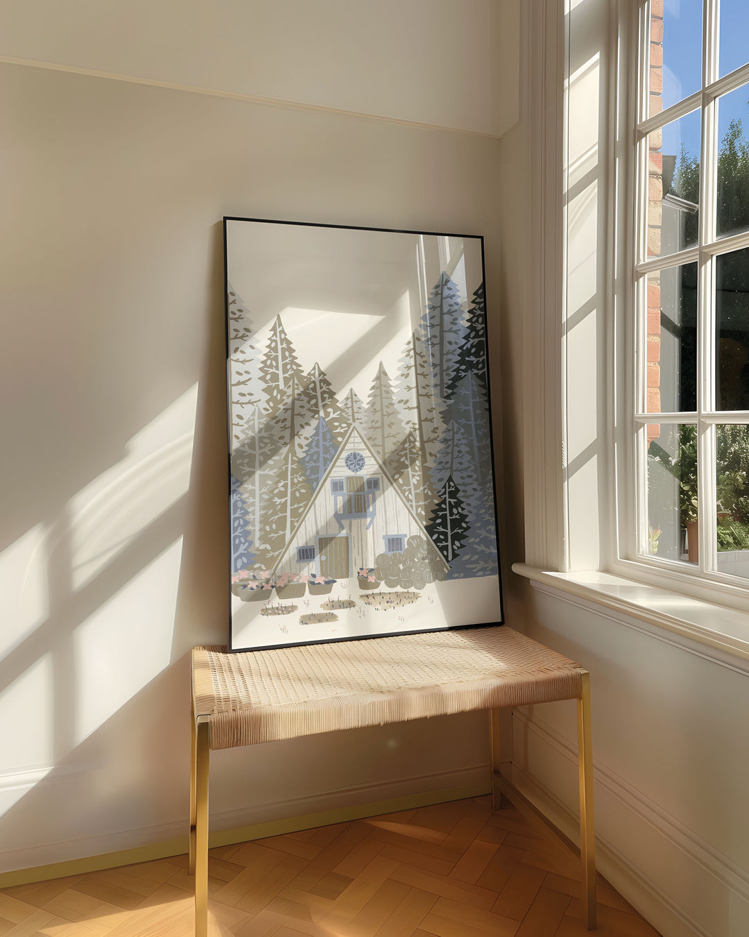 Framed Art Print titled 'Alpine Retreat' by Little Berries Studio, resting on a woven bench near a sunlit window in a bright, airy room.