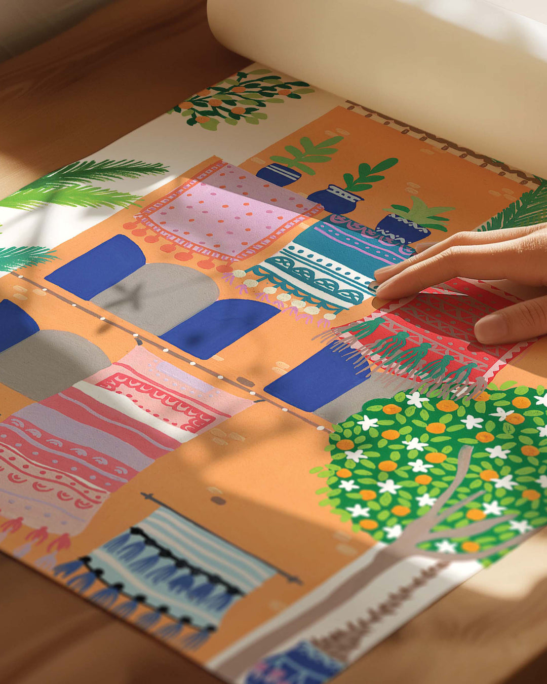 Colourful Archival Art Print of a terracotta building with vibrant rugs hanging from balconies, surrounded by lush greenery and palm trees, by Little Berries Studio.