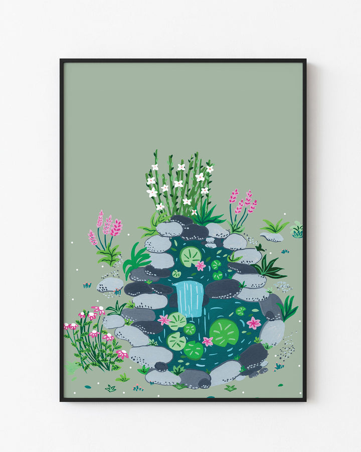 Black Framed Art Print of a small, tranquil pond surrounded by smooth stones, blooming flowers, and lush greenery by Little Berries Studio.
