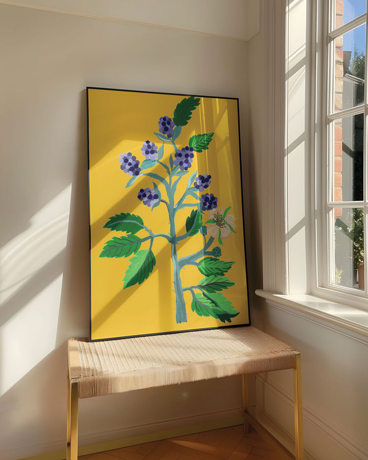 Framed Art Print titled 'Berry Blooms' by Little Berries Studio, resting on a woven bench near a sunlit window in a bright, airy room.
