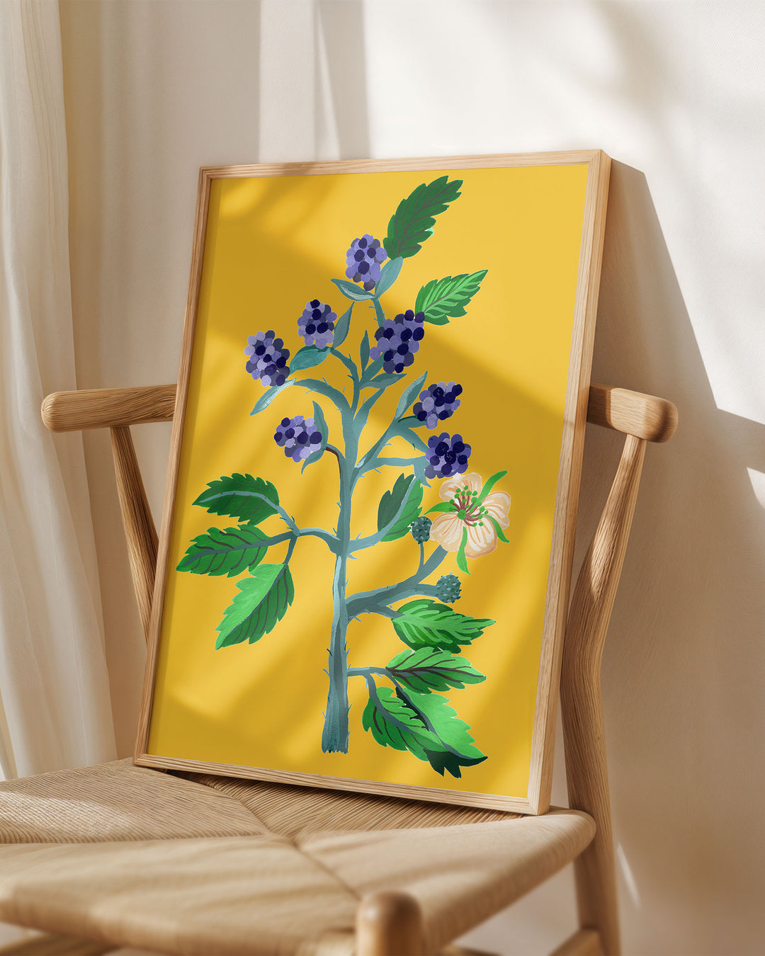 Framed Art Print titled 'Berry Blooms' by Little Berries Studio, placed on a wooden chair in a softly lit room.