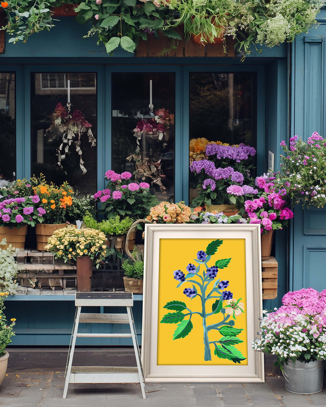 A framed Art Print by Little Berries Studio featuring a vibrant floral arrangement with blue berries and green leaves against a yellow background, displayed in front of a flower shop with various colourful plants and flowers.