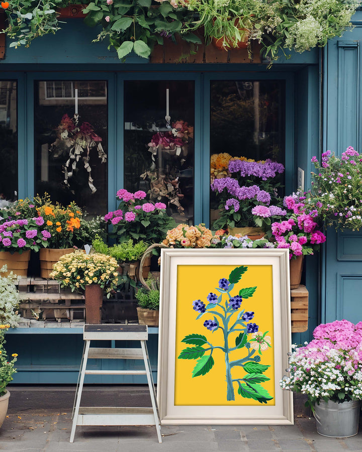A framed Art Print by Little Berries Studio featuring a vibrant floral arrangement with blue berries and green leaves against a yellow background, displayed in front of a flower shop with various colourful plants and flowers.