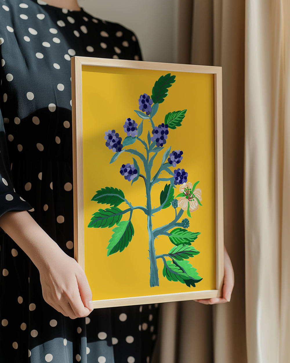 Person in a polka dot dress holding a framed botanical Art Print titled 'Berry Blooms' featuring, a flourishing plant with colourful berries and delicate flowers, created by Little Berries Studio.
