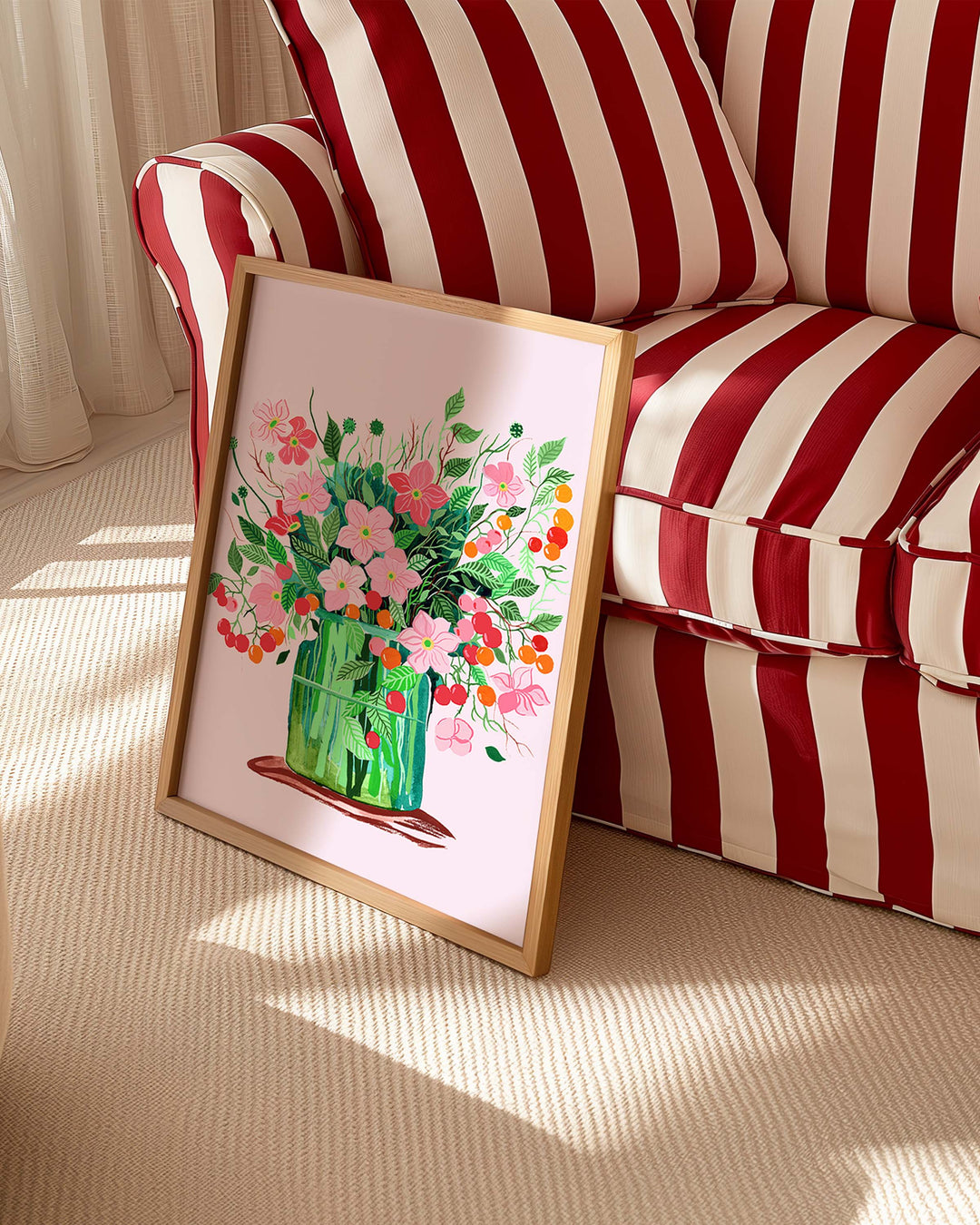 Framed Art Print titled 'Blushing Blooms' by Little Berries Studio, propped against a red and white striped sofa in a bright, sunlit room.