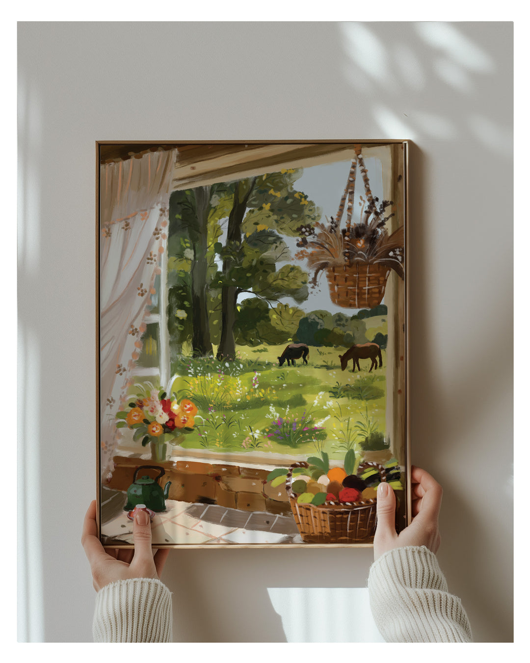 Framed artwork of a garden scene with animals and plants, held by hands against a white wall.