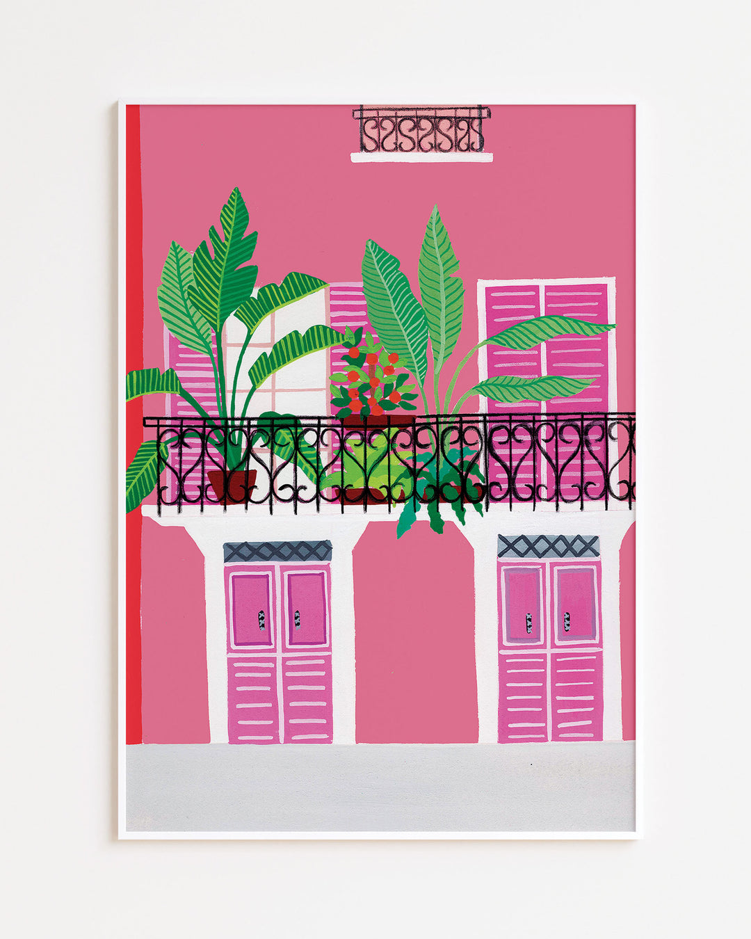 White Framed Artwork of a vibrant pink building with a black wrought-iron balcony adorned with potted tropical plants and bold pink shutters.