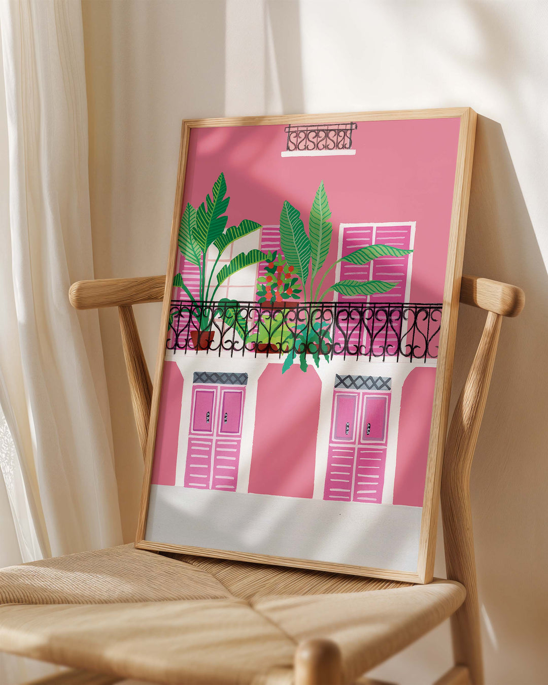 Framed Art Print titled 'Door Bloom Balcony' by Little Berries Studio, placed on a wooden chair in a softly lit room.