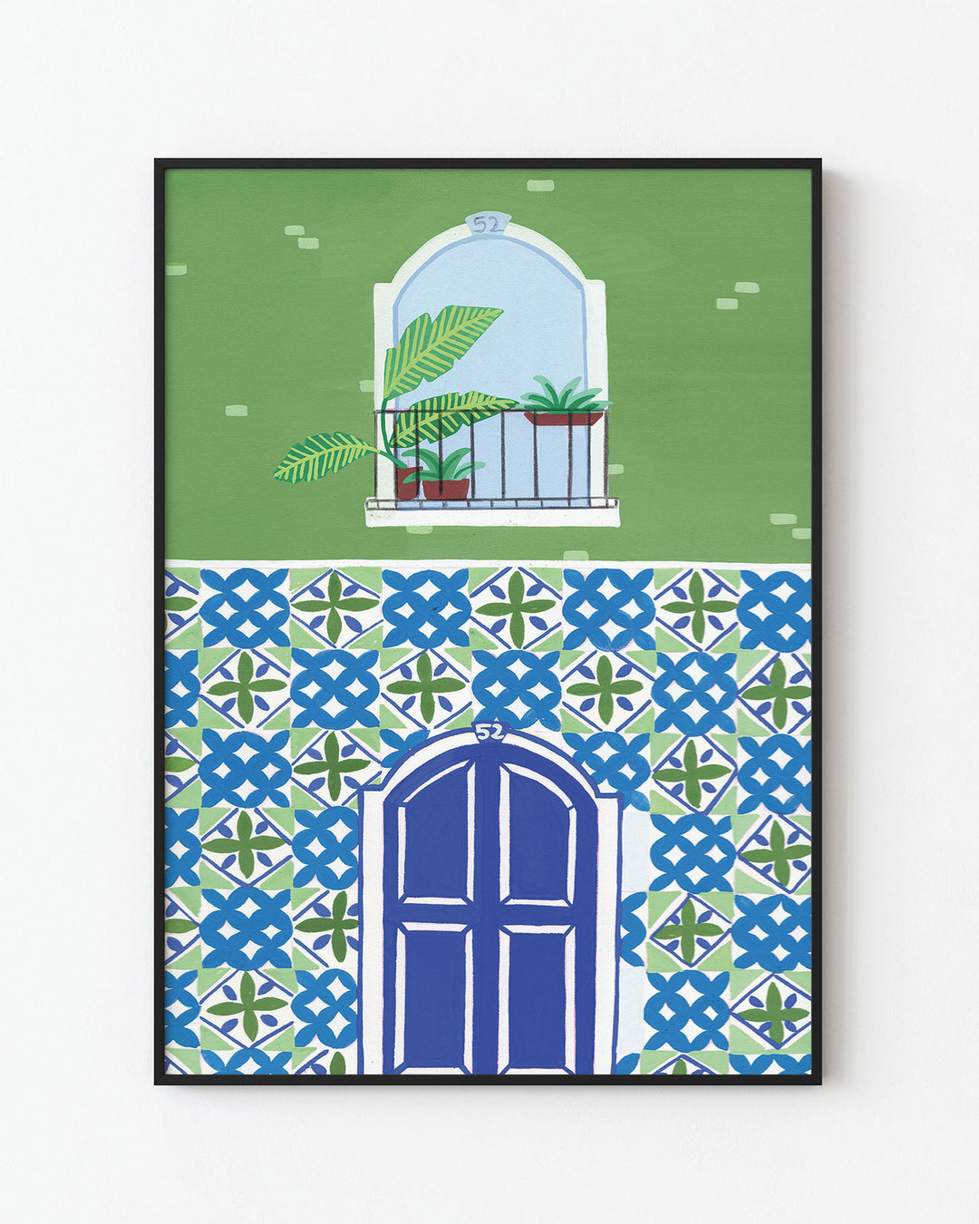 Black Framed Artwork of a Mediterranean-style building with a vibrant blue door, patterned mosaic tiles, and a small balcony featuring tropical potted plants.