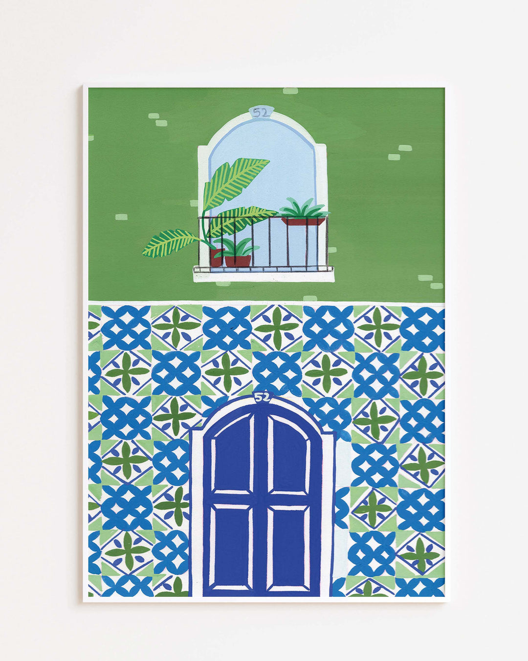 White Framed Artwork of a Mediterranean-style building with a vibrant blue door, patterned mosaic tiles, and a small balcony featuring tropical potted plants.