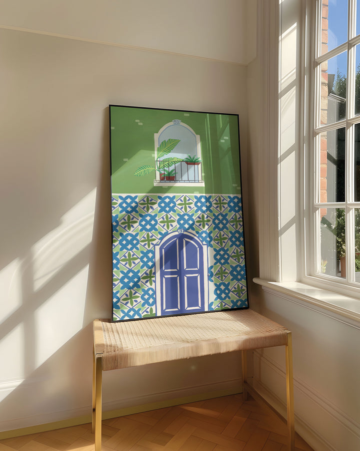 Framed Art Print titled 'Door Mediterranean Mosaic' by Little Berries Studio, resting on a woven bench near a sunlit window in a bright, airy room.
