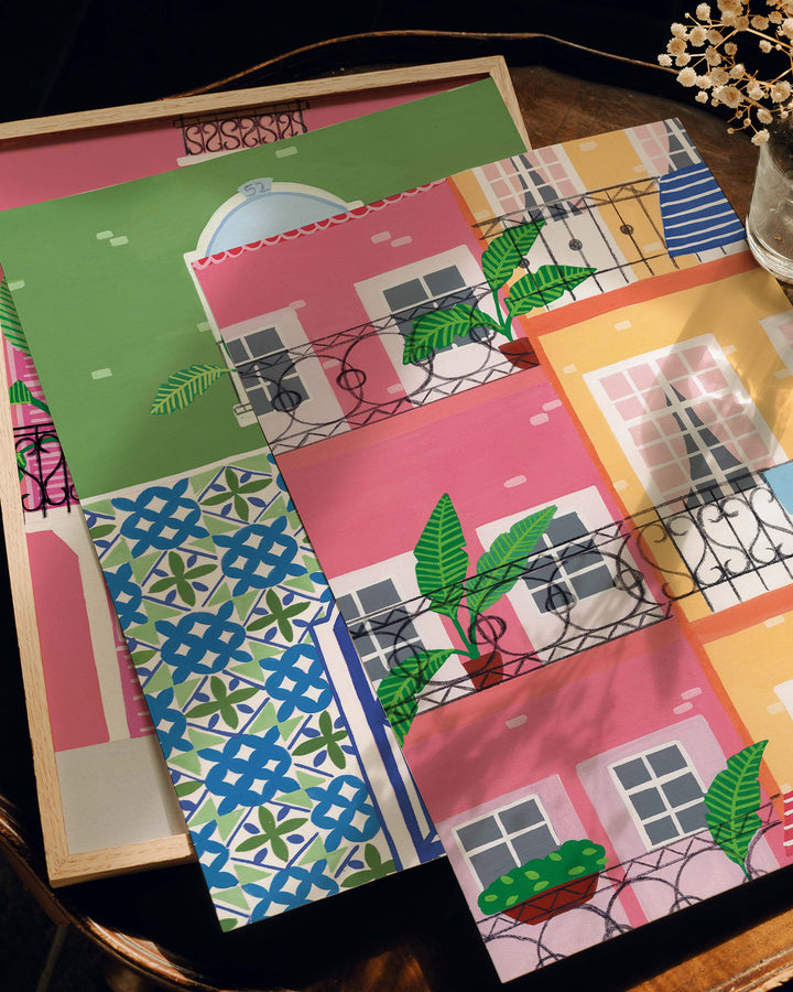 Close-up of three colourful Art Prints by Little Berries Studio featuring Mediterranean-inspired designs with pastel buildings, balconies, and intricate mosaic patterns, displayed on a wooden surface.
