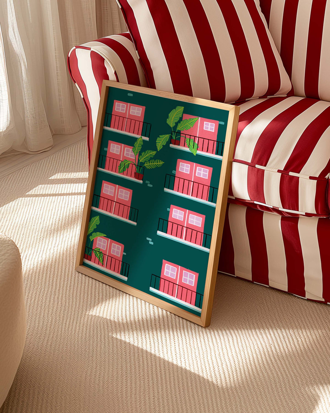 Framed Art Print titled "Door Verdant Views" by Little Berries Studio, propped against a red and white striped sofa in a bright, sunlit room.