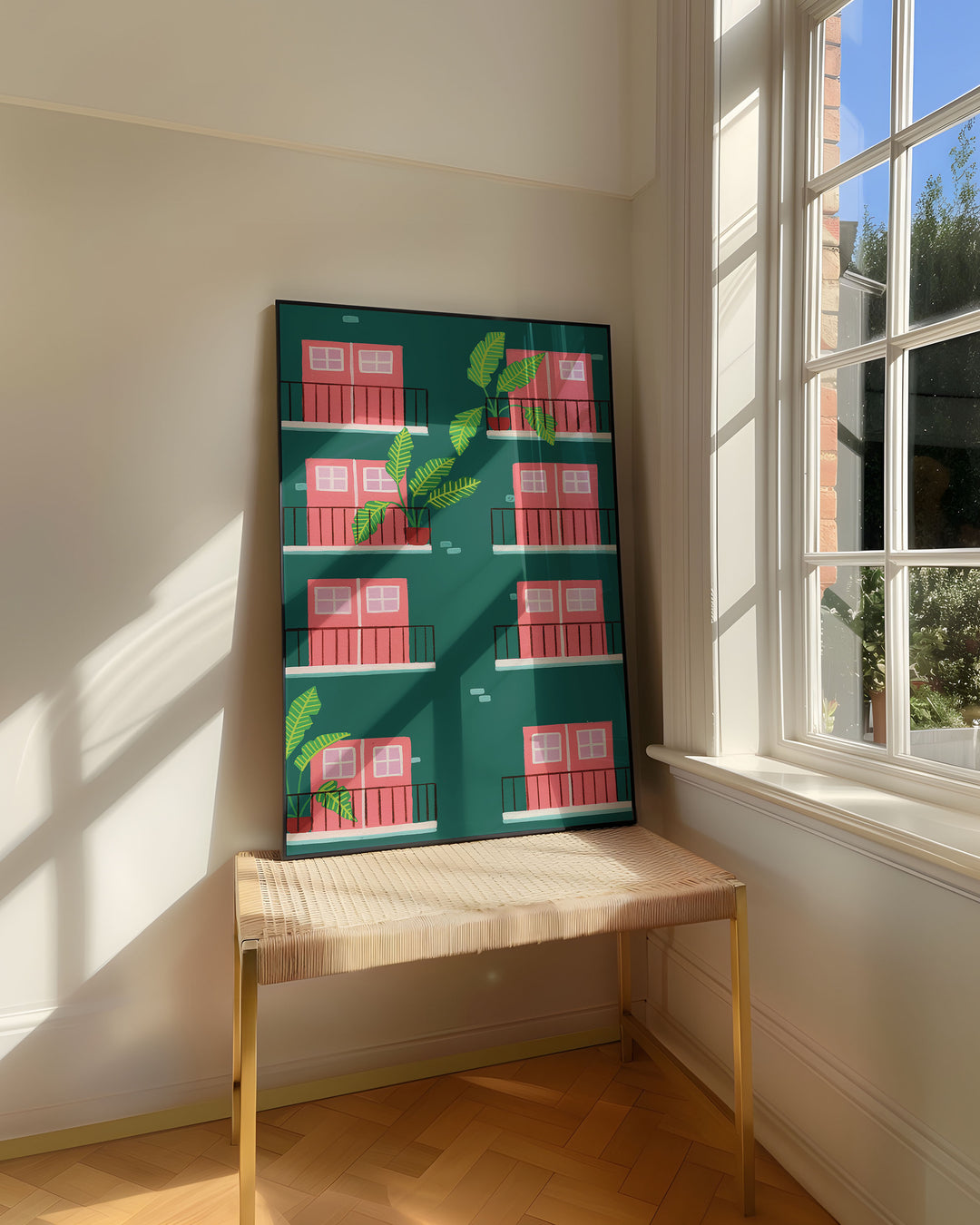 Framed Art Print titled "Door Verdant Views" by Little Berries Studio, resting on a woven bench near a sunlit window in a bright, airy room.
