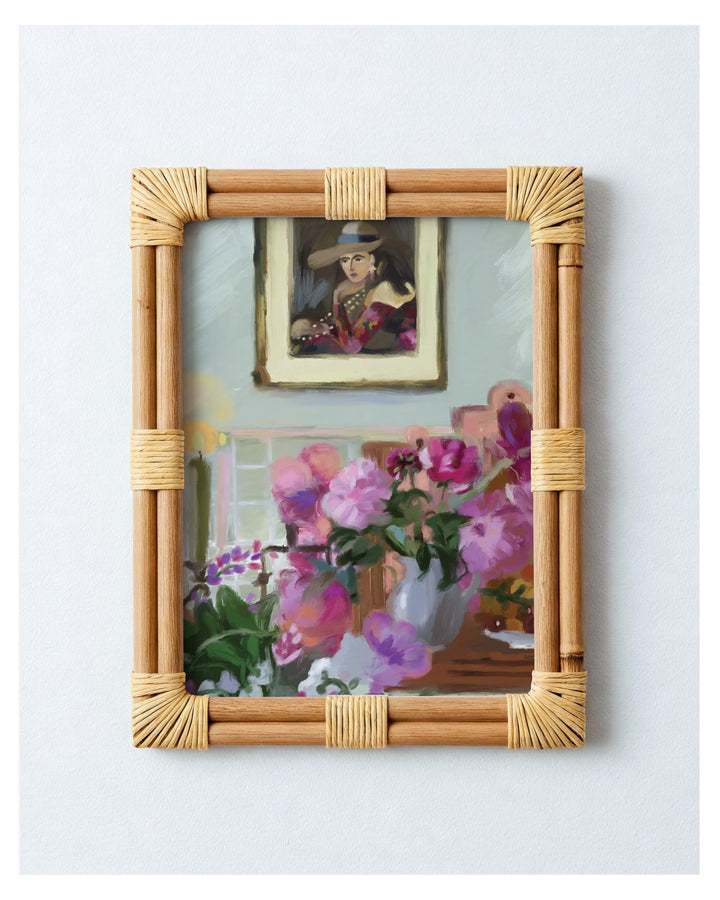 Rattan-framed artwork with floral and portrait reflection on a light blue wall