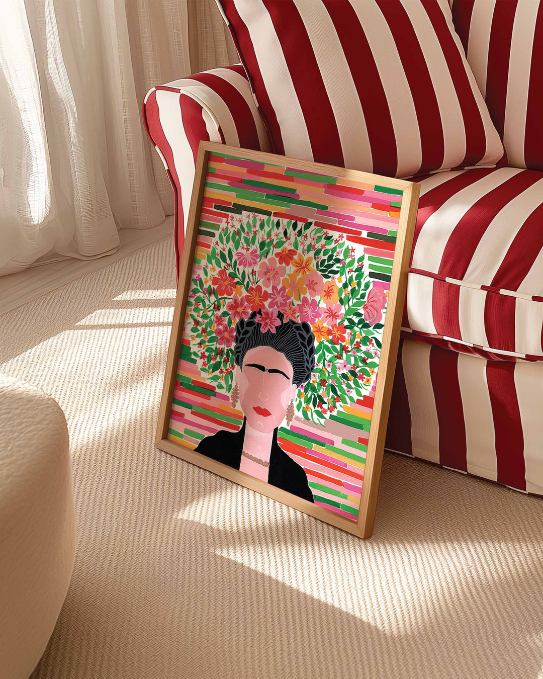 Framed Art Print titled 'Floral Frida' by Little Berries Studio, propped against a red and white striped sofa in a bright, sunlit room.