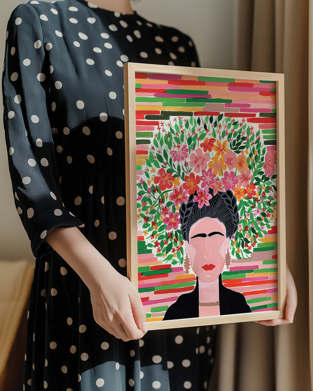 Person in a polka dot dress holding a framed botanical Art Print titled 'Floral Frida' featuring a portrait of Frida adorned with a lush floral crown, created by Little Berries Studio.