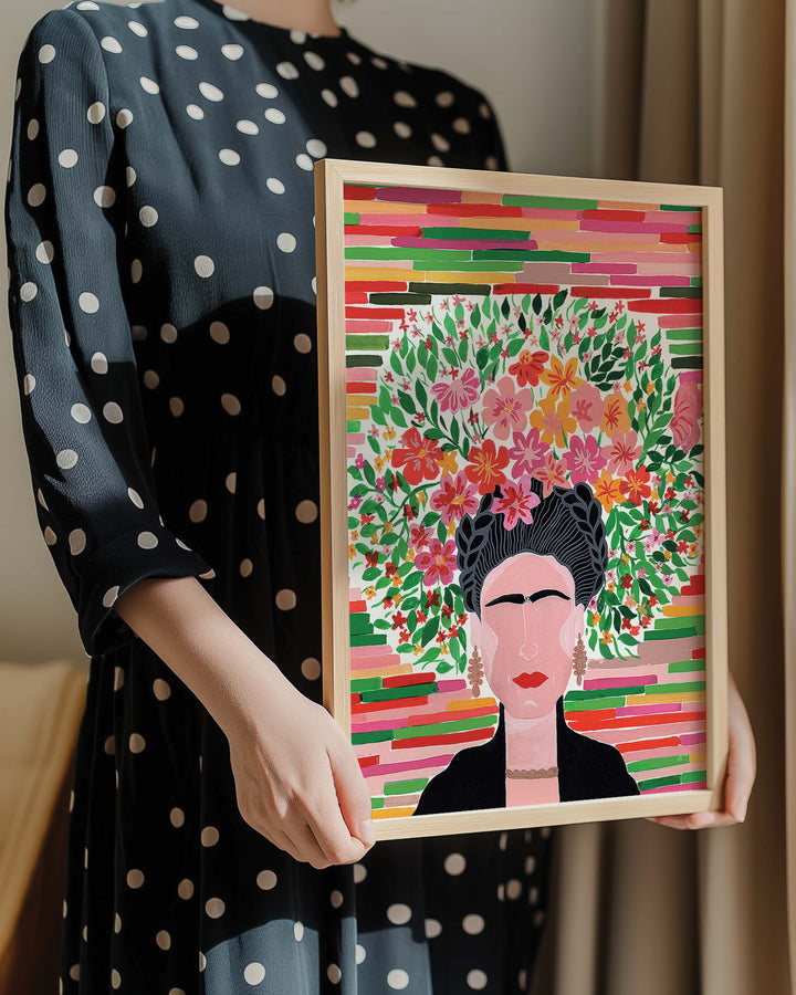 Person in a polka dot dress holding a framed botanical Art Print titled 'Floral Frida' featuring a portrait of Frida adorned with a lush floral crown, created by Little Berries Studio.