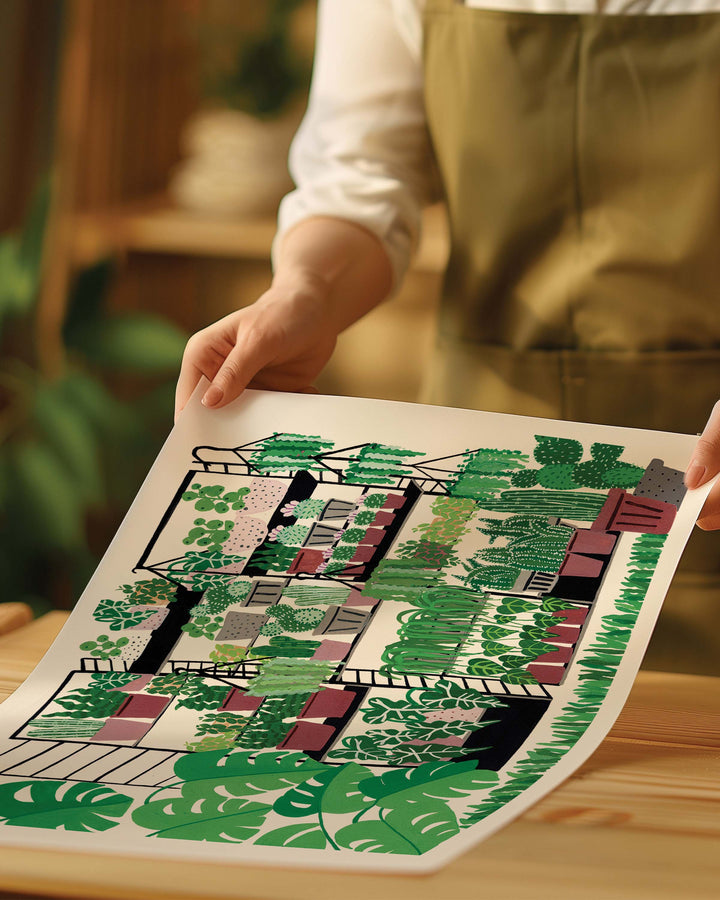 Person holding an Art Print of a variety of potted plants arranged on black metal shelves. The plants range from tall cacti to leafy tropical plants, with lush greenery filling the scene. Large monstera leaves frame the left side of the image, adding a vibrant, fresh touch to the overall composition.