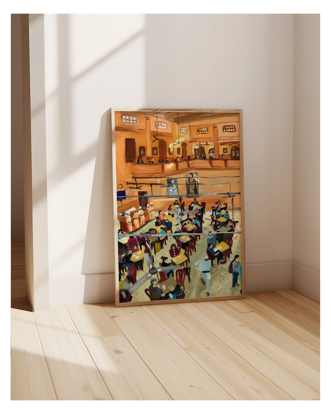 Framed artwork of a busy coffee house on a wall in a room with wooden floor and white walls.