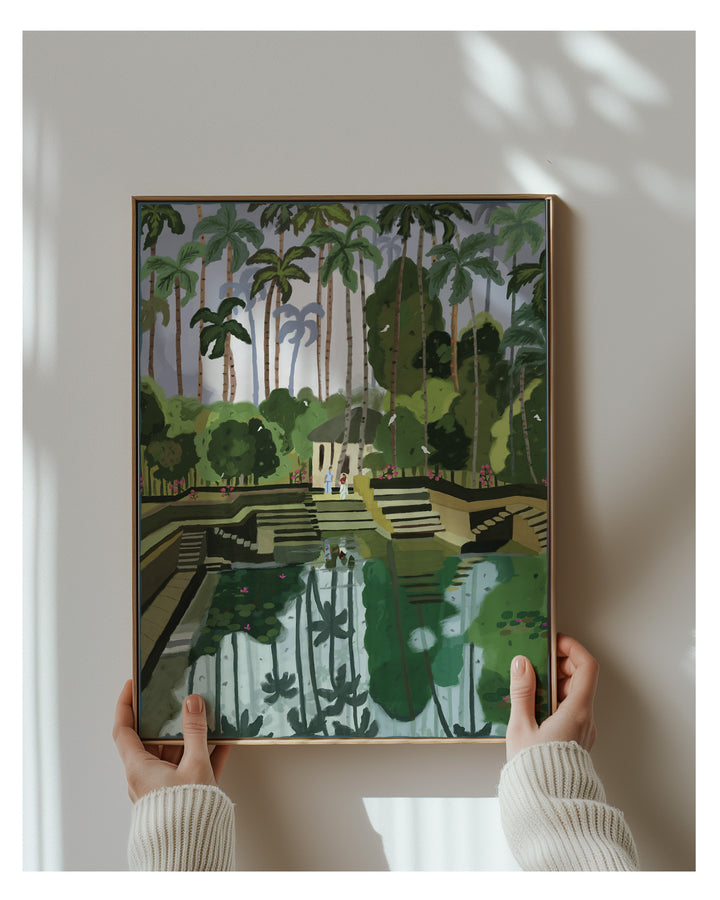 Framed artwork of a tropical Kerala landscape held by two hands against a white wall.