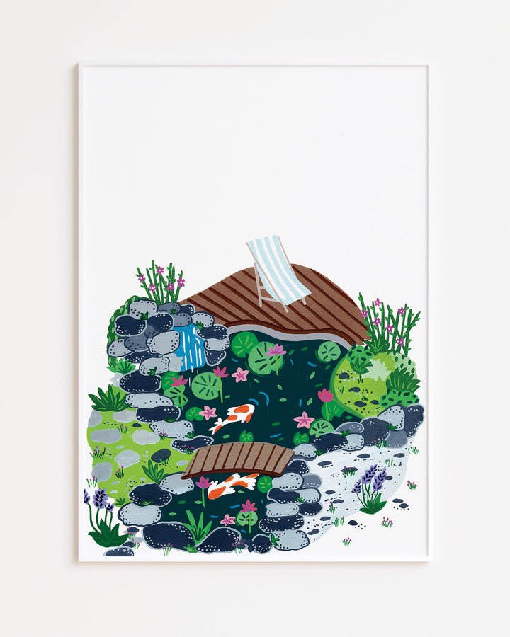 White Framed Artwork of a peaceful garden scene with a small koi pond, surrounded by rocks, blooming plants, and a wooden deck with a striped deck chair.