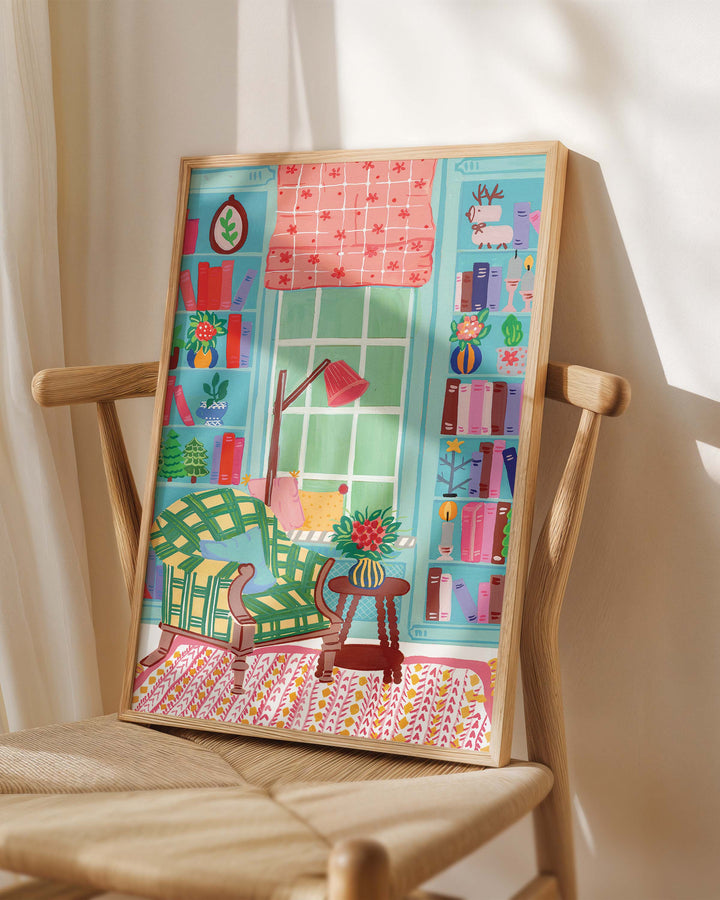 Framed Art Print titled 'Literary Retreat' by Little Berries Studio, placed on a wooden chair in a softly lit room.