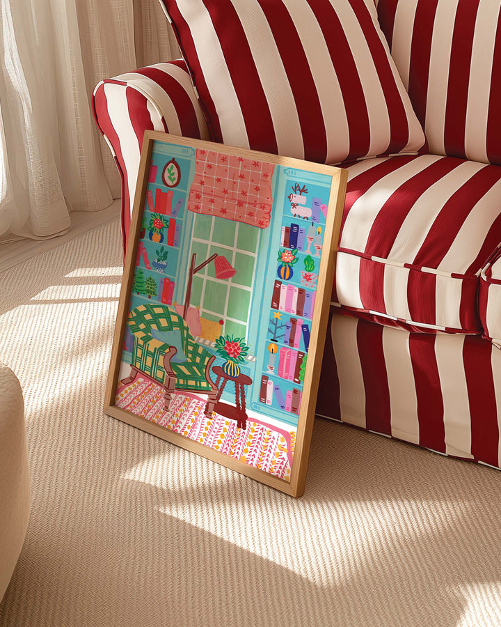 Framed Artwork titled 'Literary Retreat' by Little Berries Studio, propped against a red and white striped sofa in a bright, sunlit room.
