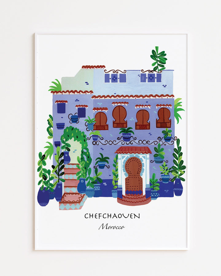 White Framed Artwork of a traditional Moroccan house in Chefchaouen by Little Berries Studio, featuring blue and white architecture, arched windows, and lush green plants.