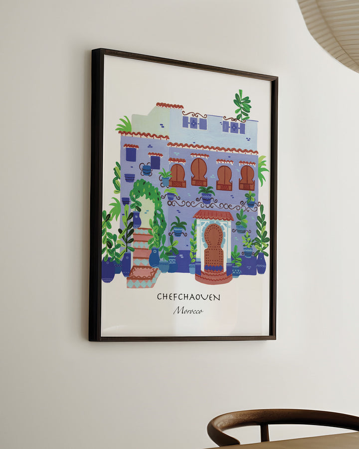 Ready-to-Hang Framed Wall Art of a traditional Moroccan house in Chefchaouen by Little Berries Studio, featuring blue and white architecture, arched windows, and lush green plants