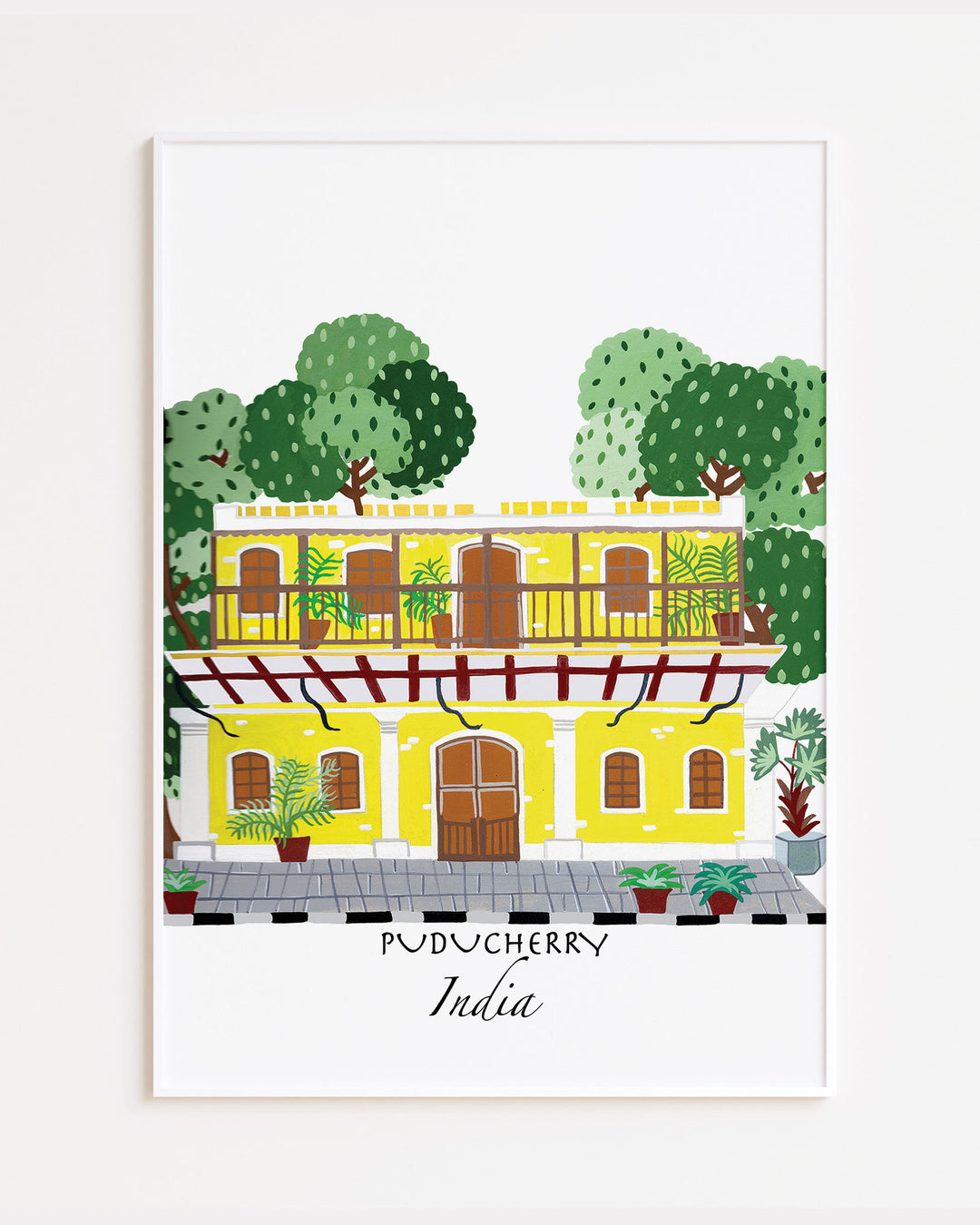 White Framed Artwork of a traditional yellow building in Puducherry, India, surrounded by lush greenery. Archival Print by Little Berries Studio.