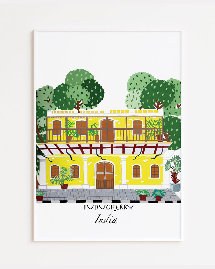 White Framed Artwork of a traditional yellow building in Puducherry, India, surrounded by lush greenery. Archival Print by Little Berries Studio.