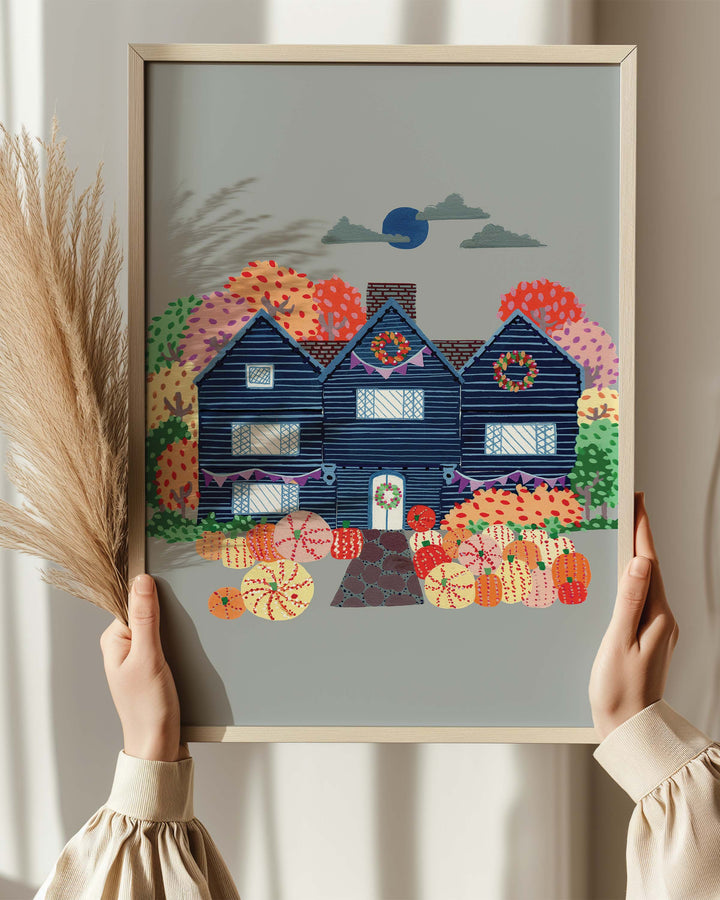 Person holding an Artwork of a cosy, orange Victorian house surrounded by trees, capturing the essence of autumn with festive details and warm seasonal colours.