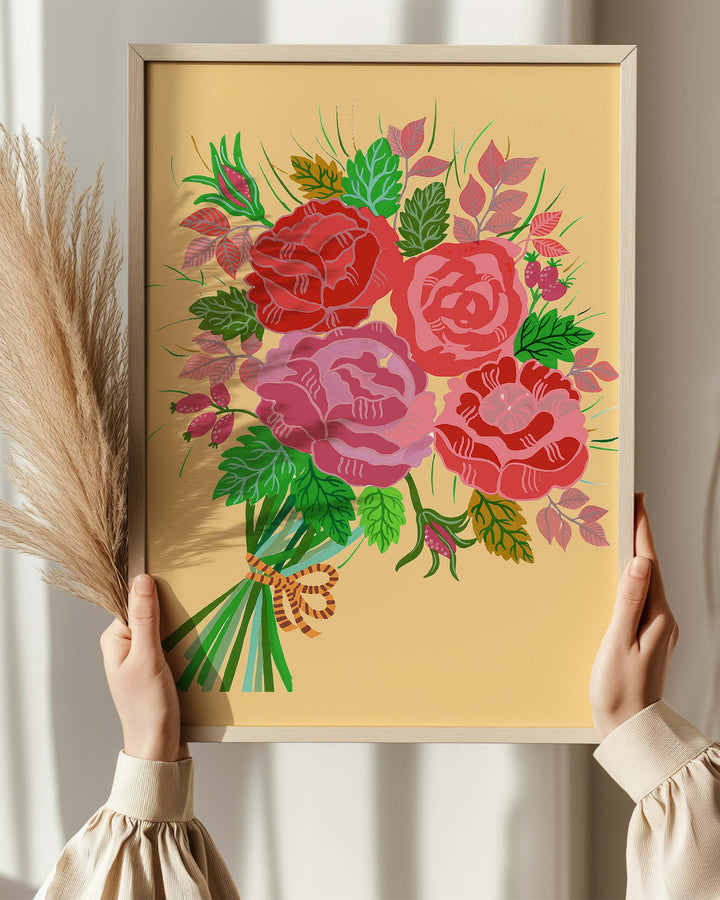 Beautiful hands holding a Framed Artwork featuring a bouquet of red and pink roses with lush green leaves and delicate accents on a warm yellow background, created by Little Berries Studio.