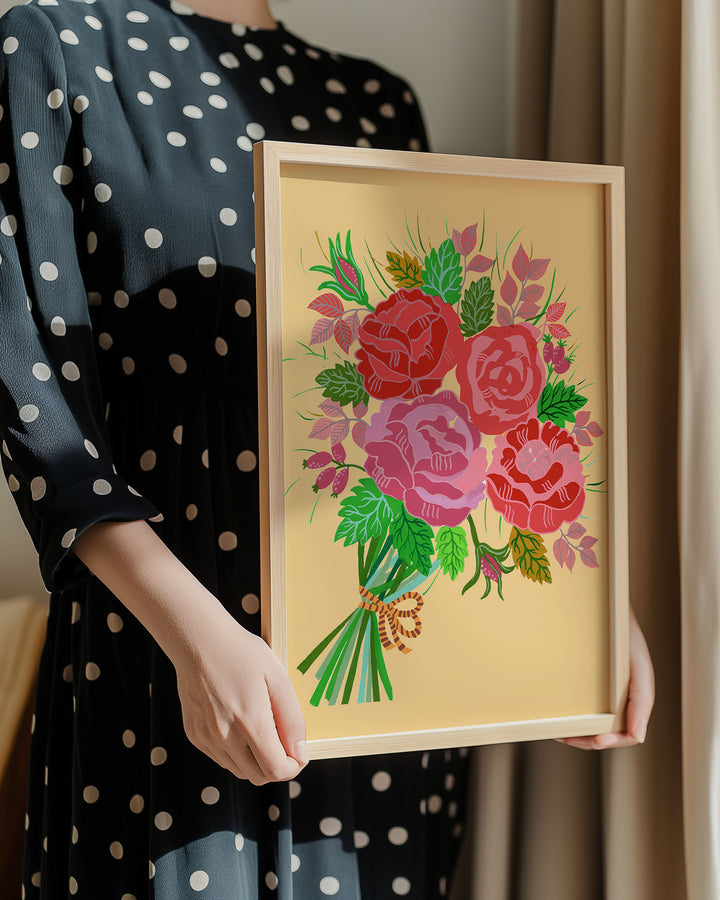A lady in a polka dot dress holding a Framed Artwork featuring a bouquet of red and pink roses with lush green leaves and delicate accents on a warm yellow background, created by Little Berries Studio.