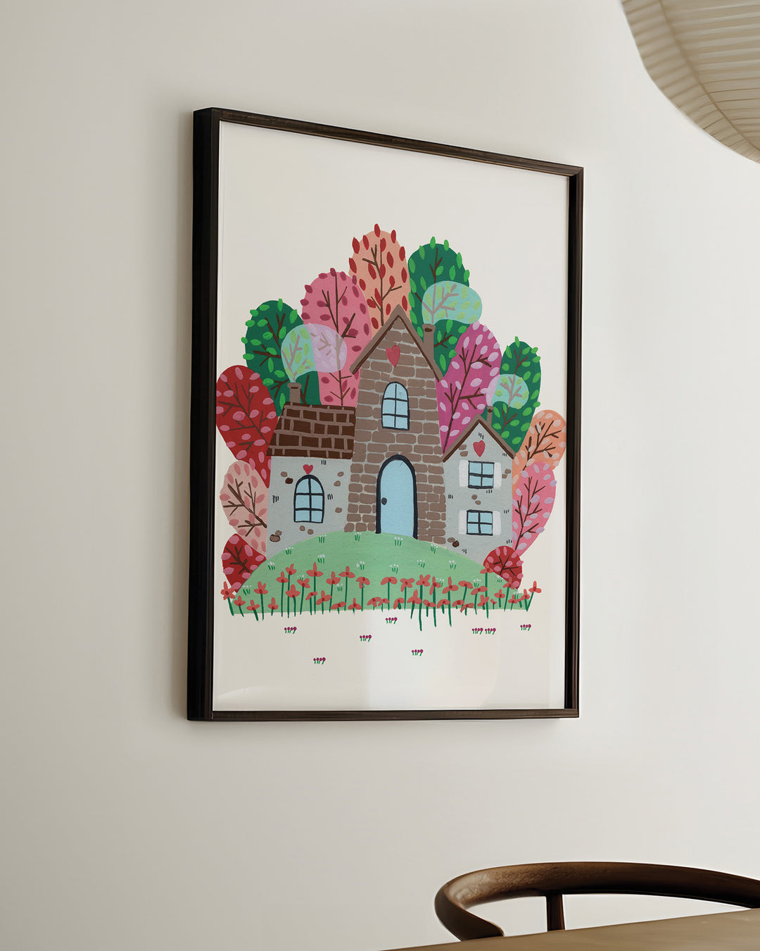Ready-to-Hang Framed Wall Art of a cozy Smoke House with a blue door and heart details, surrounded by vibrant, colourful trees and blooming red flowers, ideal for decorating kids' rooms.