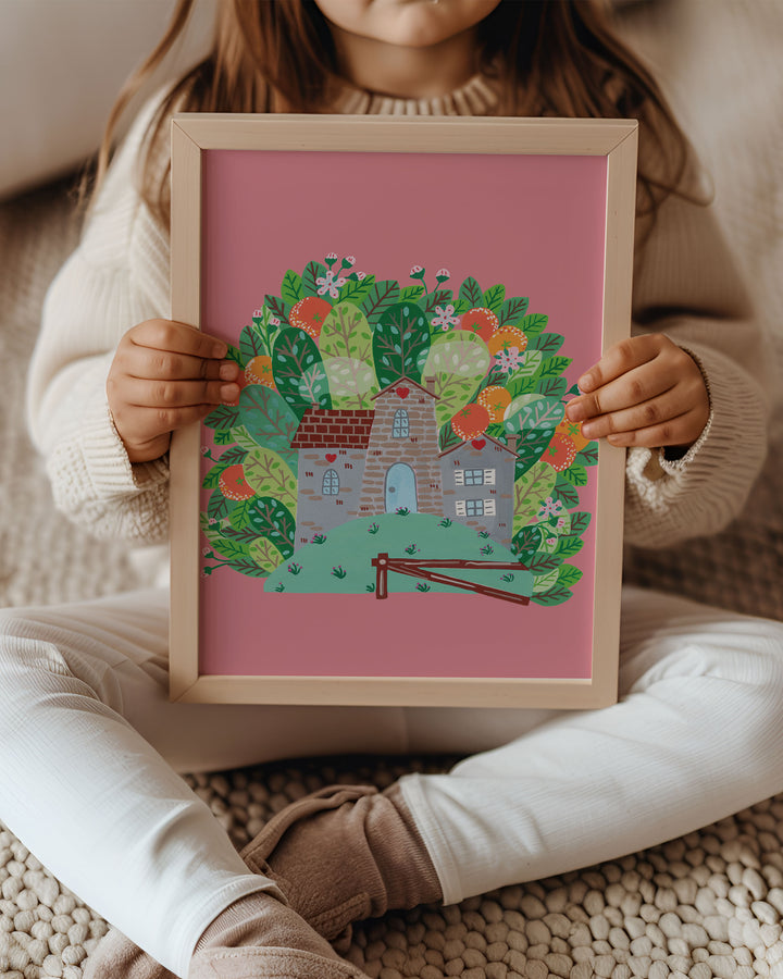A little girl holding Framed Artwork of a cozy Smoke House with a blue door and heart details, surrounded by vibrant, blooming foliage on a pink background, ideal for decorating kids rooms.