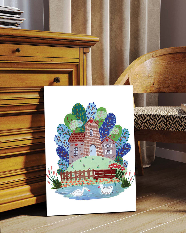 Framed Art Print titled 'Smokehouse Lakeside Serenity' by Little Berries Studio, featuring a stone house by a lake with swans, propped against a wooden dresser in a cozy room setting.