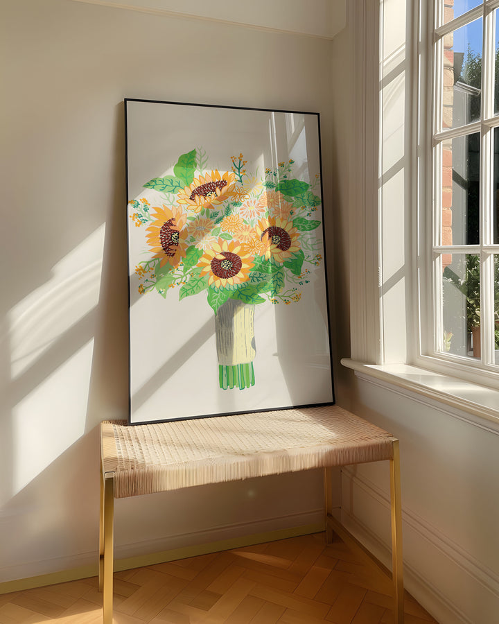 Framed Art Print titled 'Sunny Serenade' by Little Berries Studio, resting on a woven bench near a sunlit window in a bright, airy room.