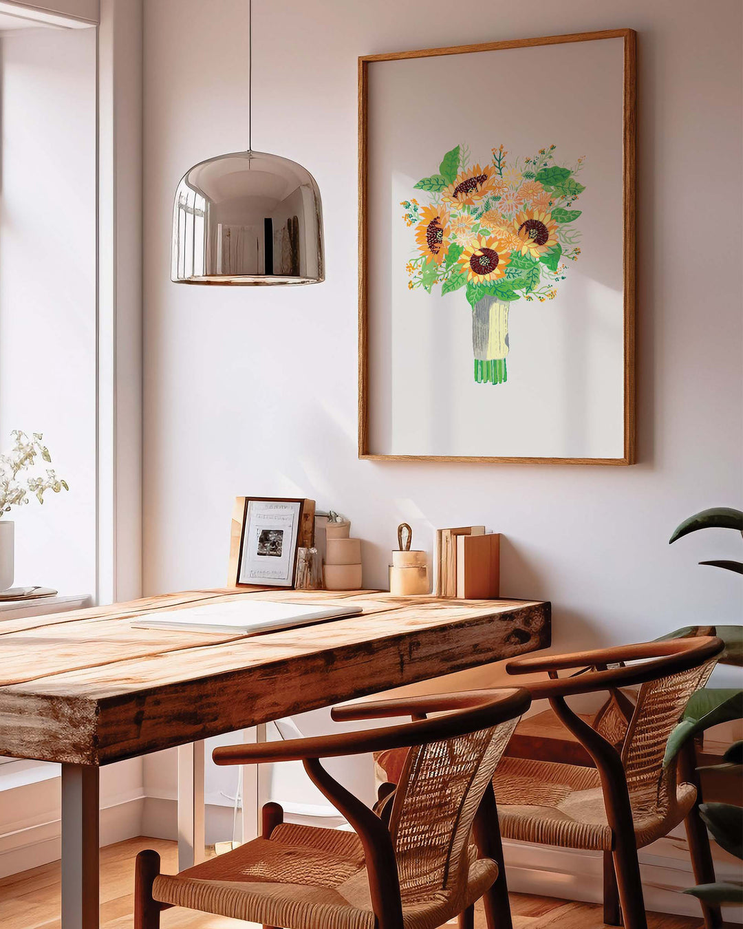  Framed Art Print by Little Berries Studio, titled 'Sunny Serenade,' featuring a vibrant bouquet of sunflowers and assorted flowers with green leaves, displayed in a stylish, sunlit dining room with wooden furniture and a modern pendant light.