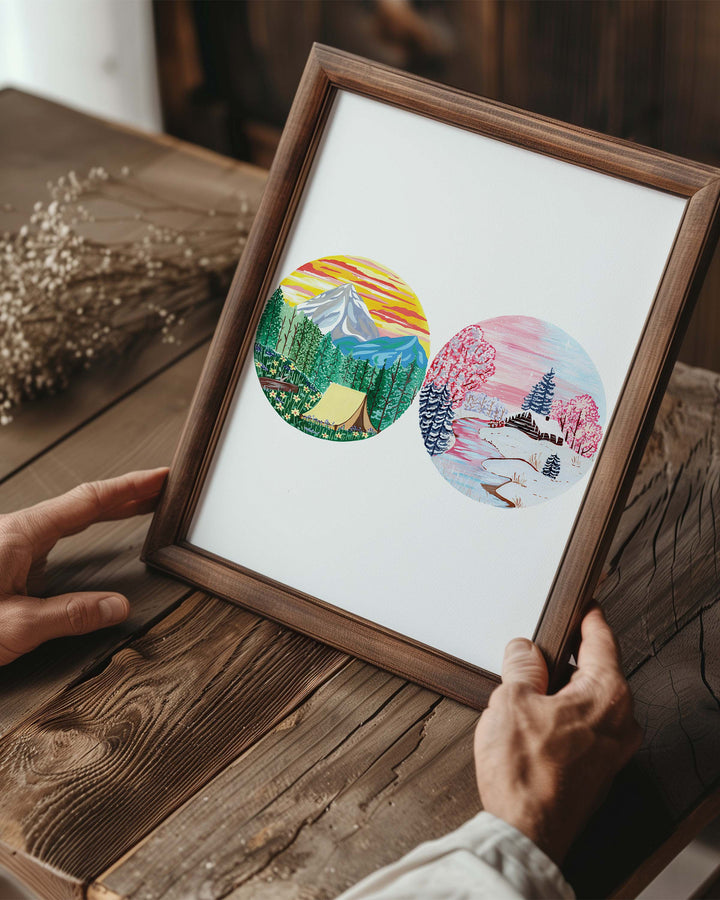 Person holding a Framed Art Print of two circular nature illustrations: one with a tent in a forest, the other depicting a snowy winter cabin, created by Little Berries Studio.