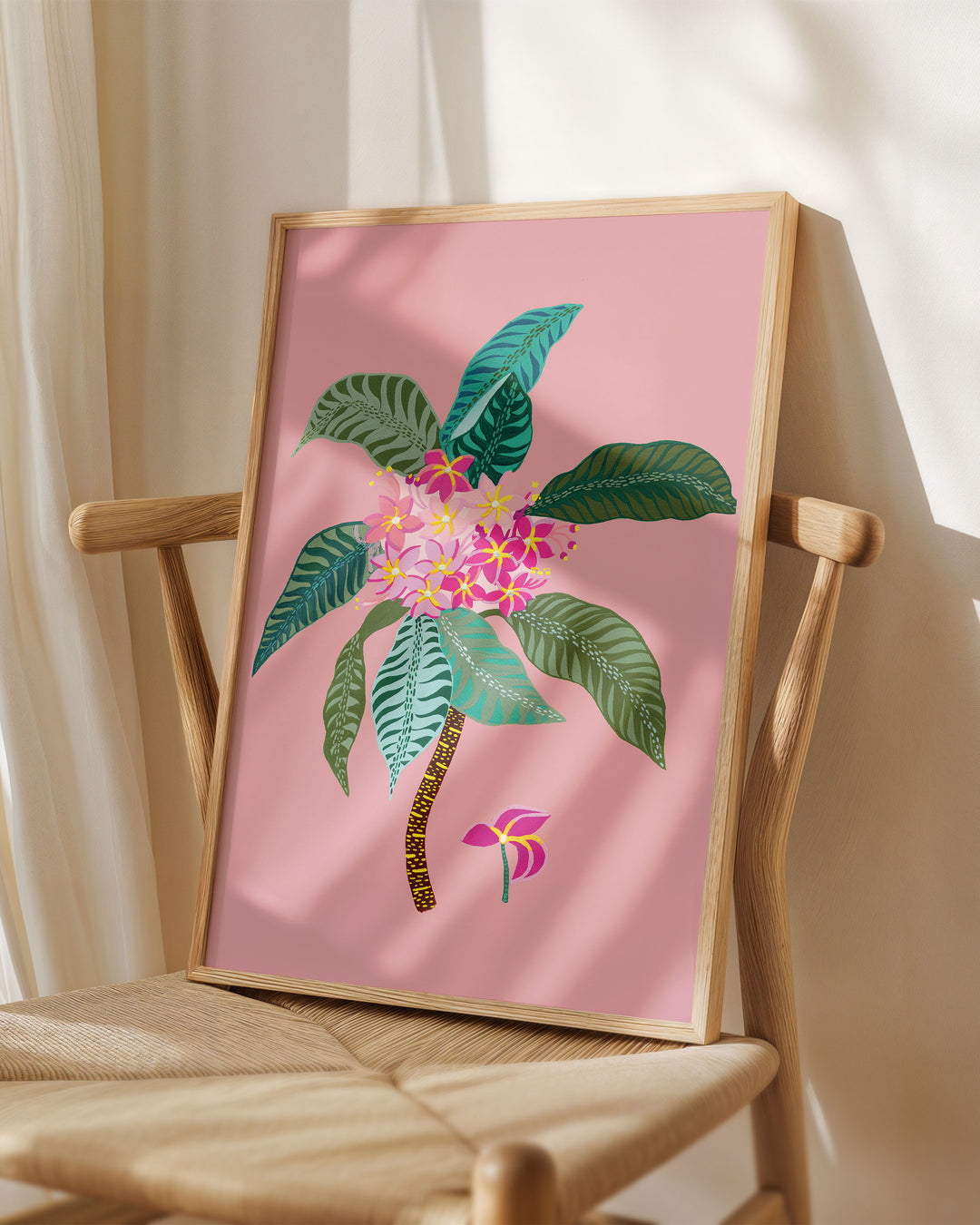 Framed Art Print titled 'Tropical Bouquet' by Little Berries Studio, placed on a wooden chair in a softly lit room.