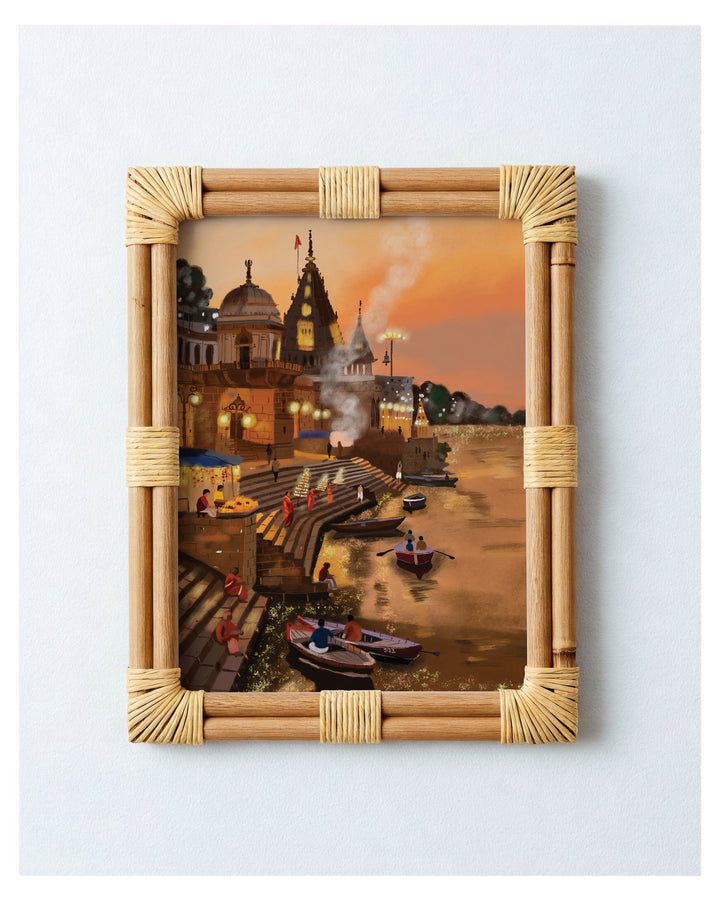 Framed artwork of a temple by a Varanasi ghat  with people and boats, set against an orange sky.