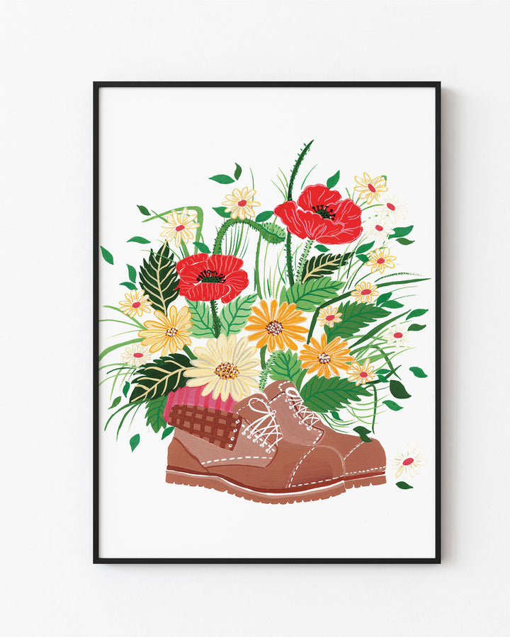 Black Framed Artwork, titled 'Wildflower Walk' features a brown hiking boot filled with an array of vibrant wildflowers, including red poppies, yellow daisies, and other colourful blossoms.