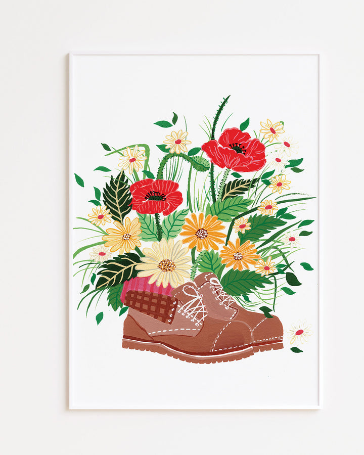 White Framed Artwork, titled 'Wildflower Walk' features a brown hiking boot filled with an array of vibrant wildflowers, including red poppies, yellow daisies, and other colourful blossoms.