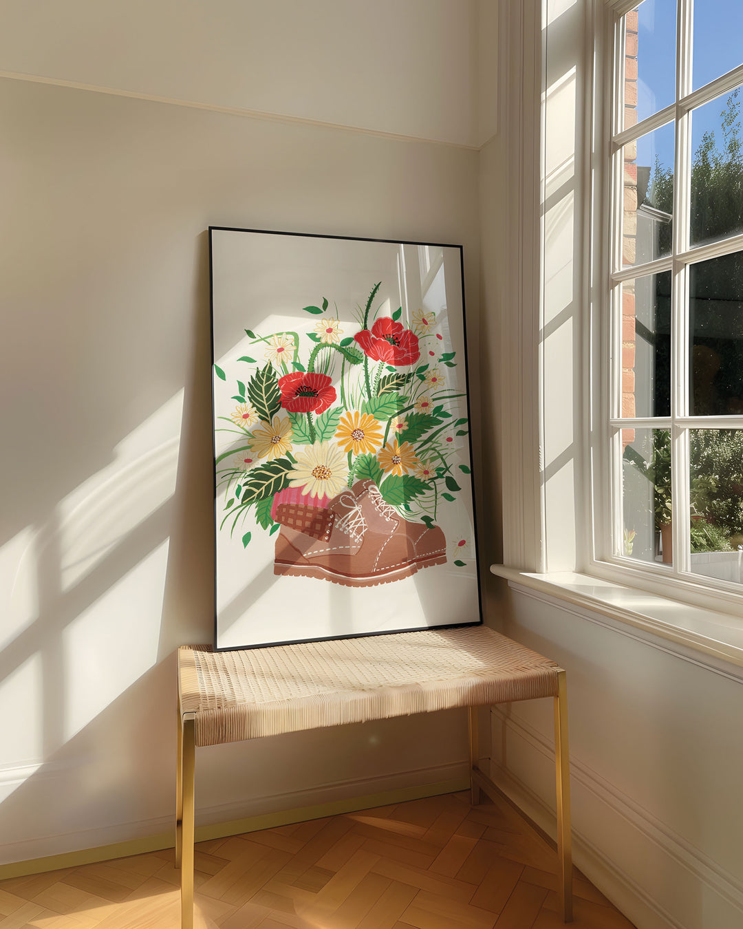 Framed Art Print titled 'Wildflower Walk' by Little Berries Studio, resting on a woven bench near a sunlit window in a bright, airy room.