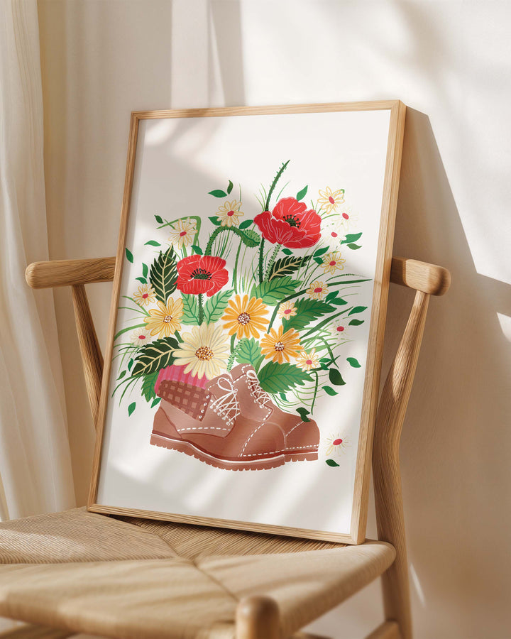 Framed Art Print titled 'Wildflower Walk' by Little Berries Studio, placed on a wooden chair in a softly lit room.