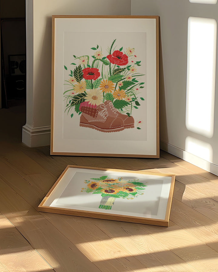 The Print is framed in a simple wooden frame, features a brown hiking boot filled with an array of vibrant wildflowers, including red poppies, yellow daisies, and other colourful blossoms.
