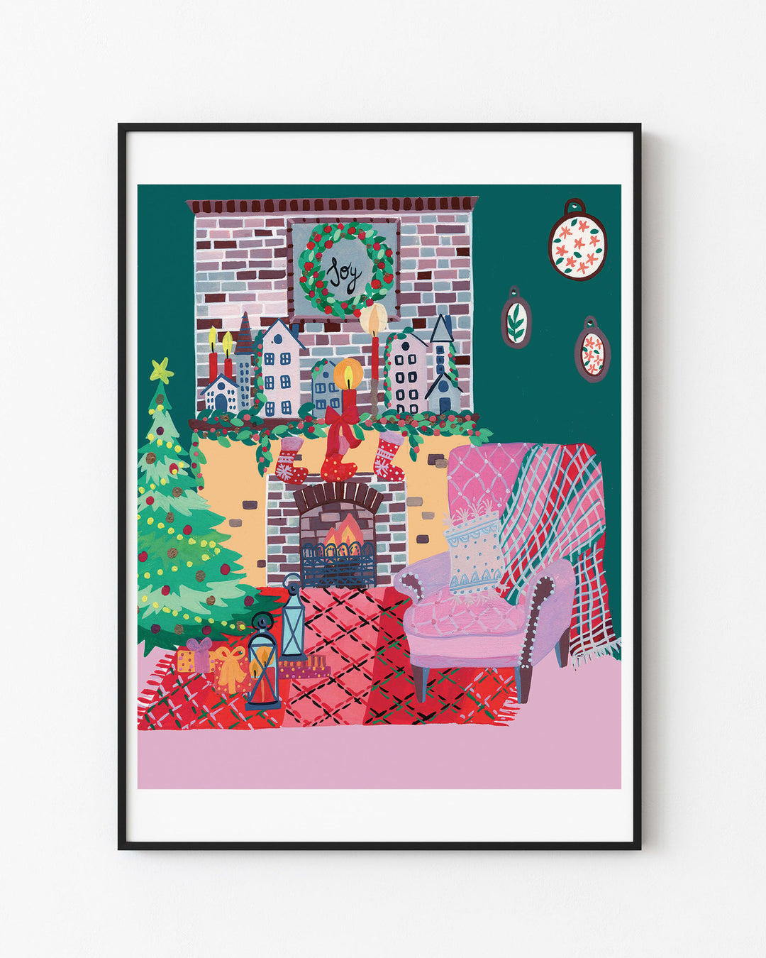 Black Framed Artwork of a cozy holiday living room with a decorated Christmas tree, stockings hanging over a brick fireplace, a wreath with 'Joy' above the mantel, and a comfy armchair with a pink and red plaid rug.