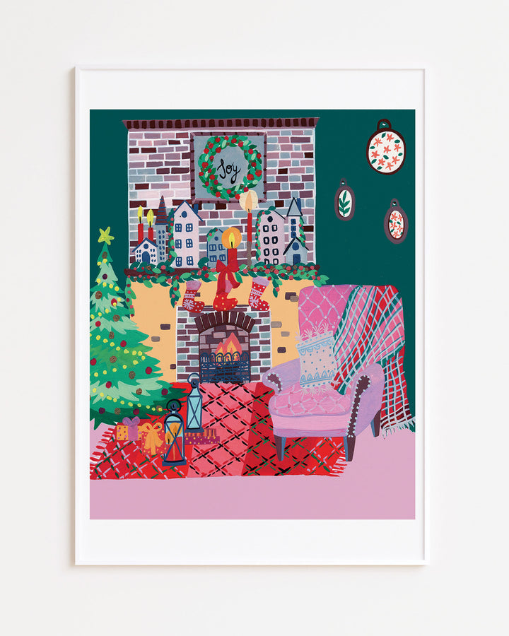 White Framed Artwork of a cozy holiday living room with a decorated Christmas tree, stockings hanging over a brick fireplace, a wreath with 'Joy' above the mantel, and a comfy armchair with a pink and red plaid rug.